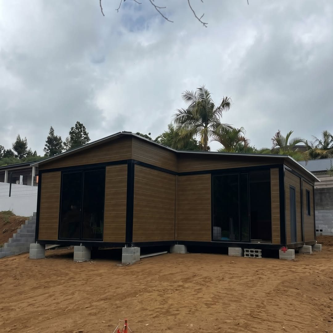 Maison modulaire Kaz'Foxy à bardage effet bois et baies vitrées noires, posée sur plots béton aux Makes